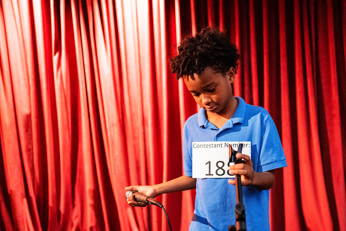 A student holding a microphone standing on a stage. The student appears to be nervous.