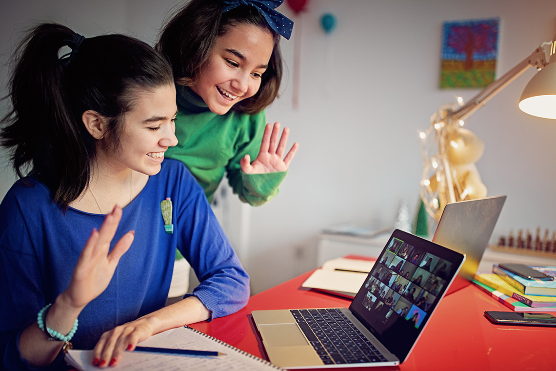 Learners waving at the camera on a computer that is displaying a video call with many other learners
