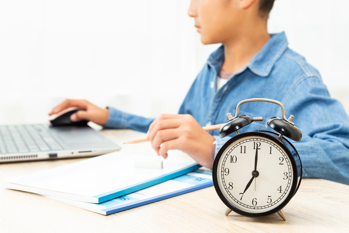 A learner working on a computer next to an alarm clock