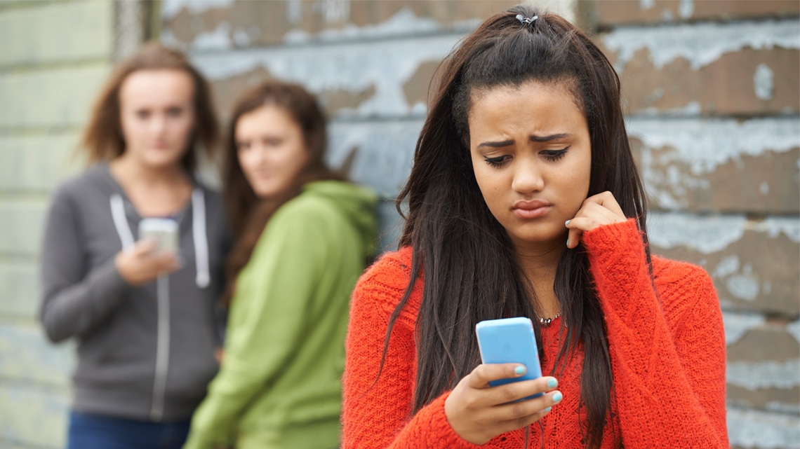 A learner looking at their smartphone and frowning while 2 other learners stare and point at them