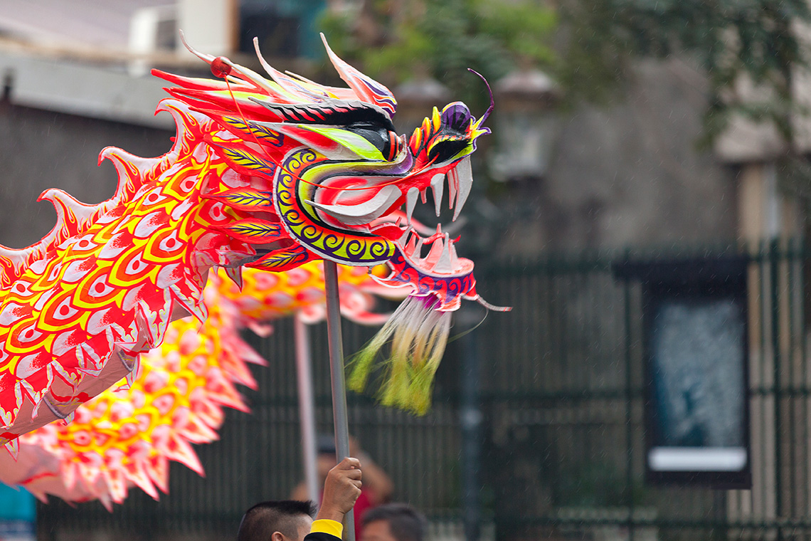 A dancer at an outdoor festival using a pole to raise the head of a dragon puppet.
