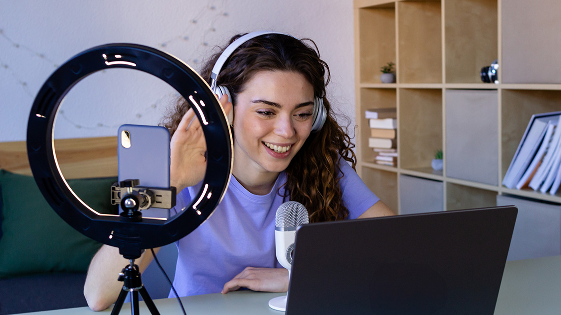 A person recording and filming for a podcast using a laptop, ring camera, and a microphone.