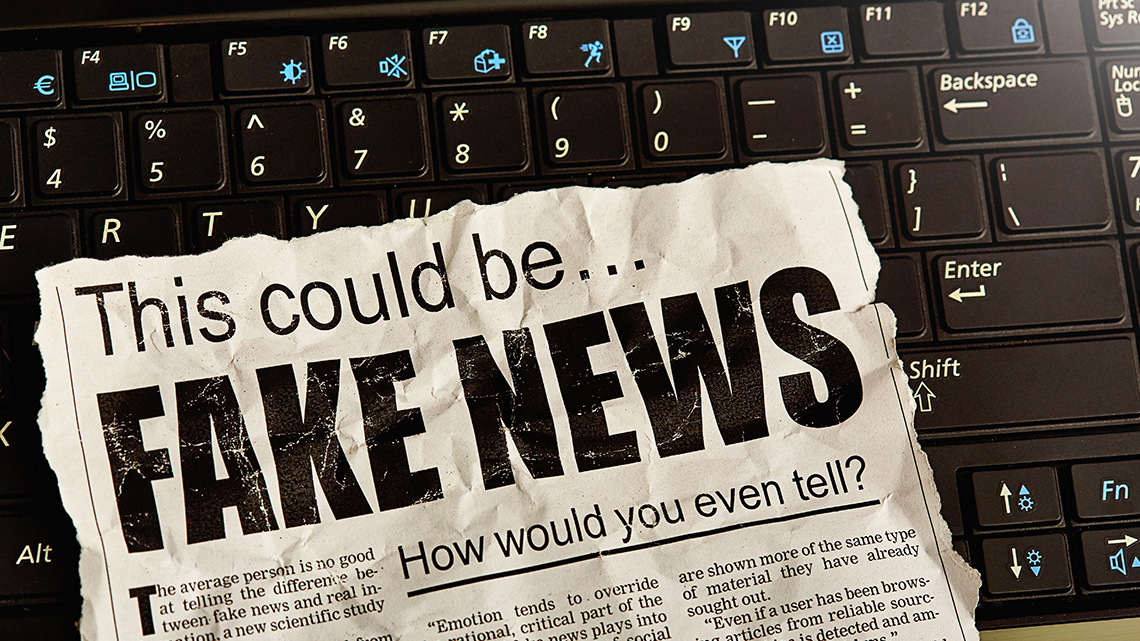 A laptop keyboard with a newspaper on top that reads: "This could be…FAKE NEWS. How would you even tell?"
