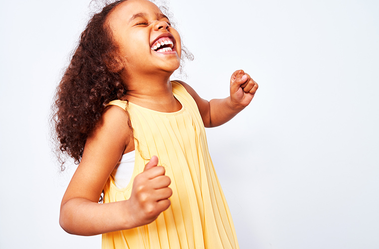 A young girl smiling and laughing with her eyes closed, her hands clenched into fists, and her arms half raised