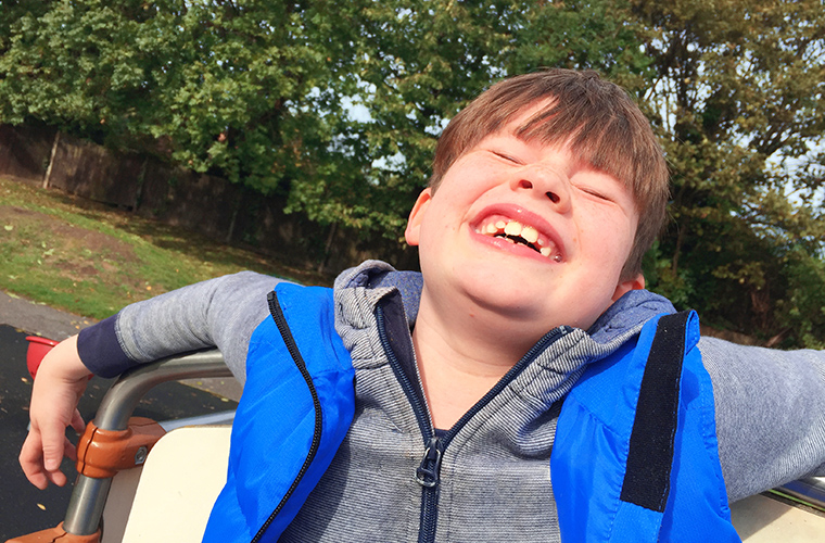 A young boy sitting back with his head tilted and his eyes closed as he smiles.