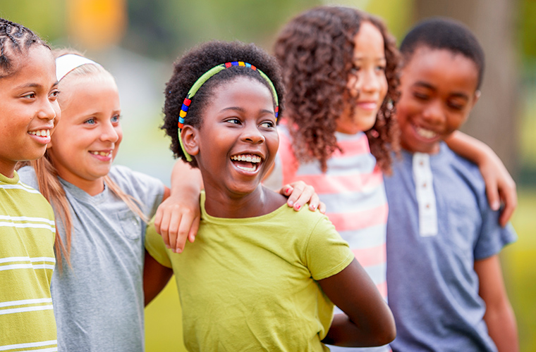 A group of children smiling with their arms around each other.