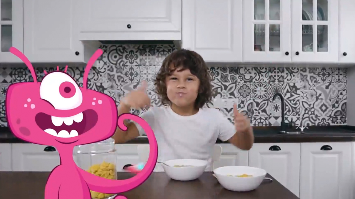 An image from the Space Puffs cereal video with a kid eating the cereal and giving two thumbs up. The cartoon alien is smiling at the kid.
