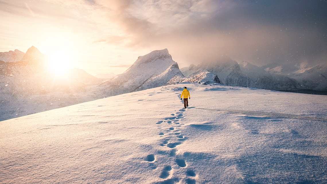 A person walking through fresh snow in the sunshine, leaving a trail of footprints behind them.