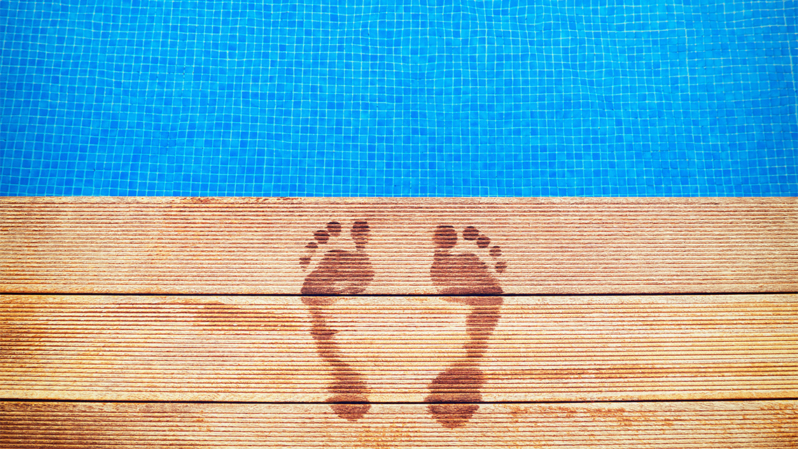 Footprints on a wooden surface with blue swimming pool in the background.