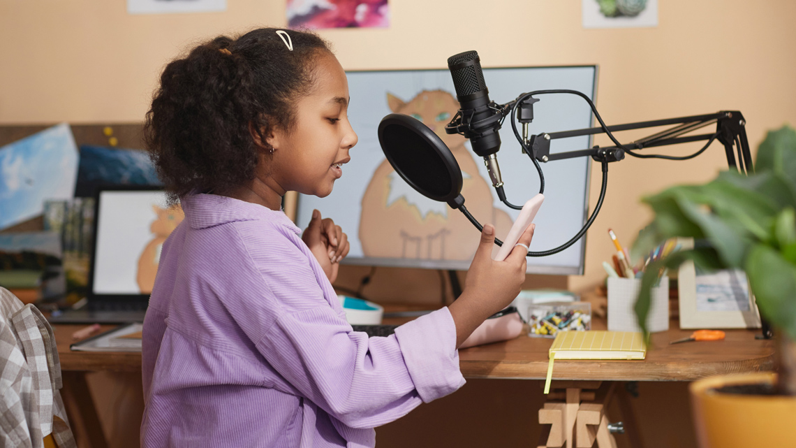 A child recording audio into a microphone connected to a computer on their desk