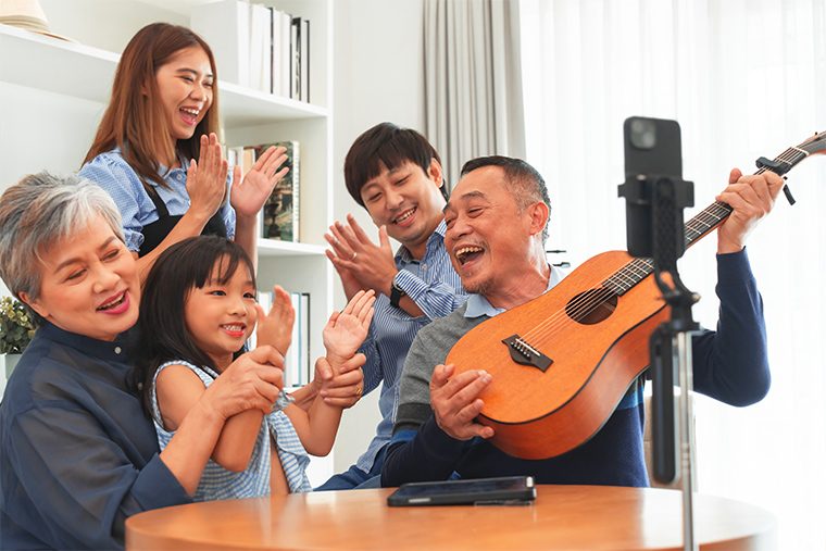 One person plays a guitar while a child and adults of different ages are clapping and singing.
