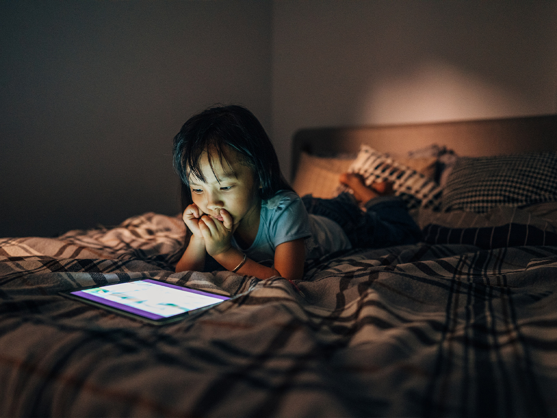 A young girl reading on a tablet in the dark.