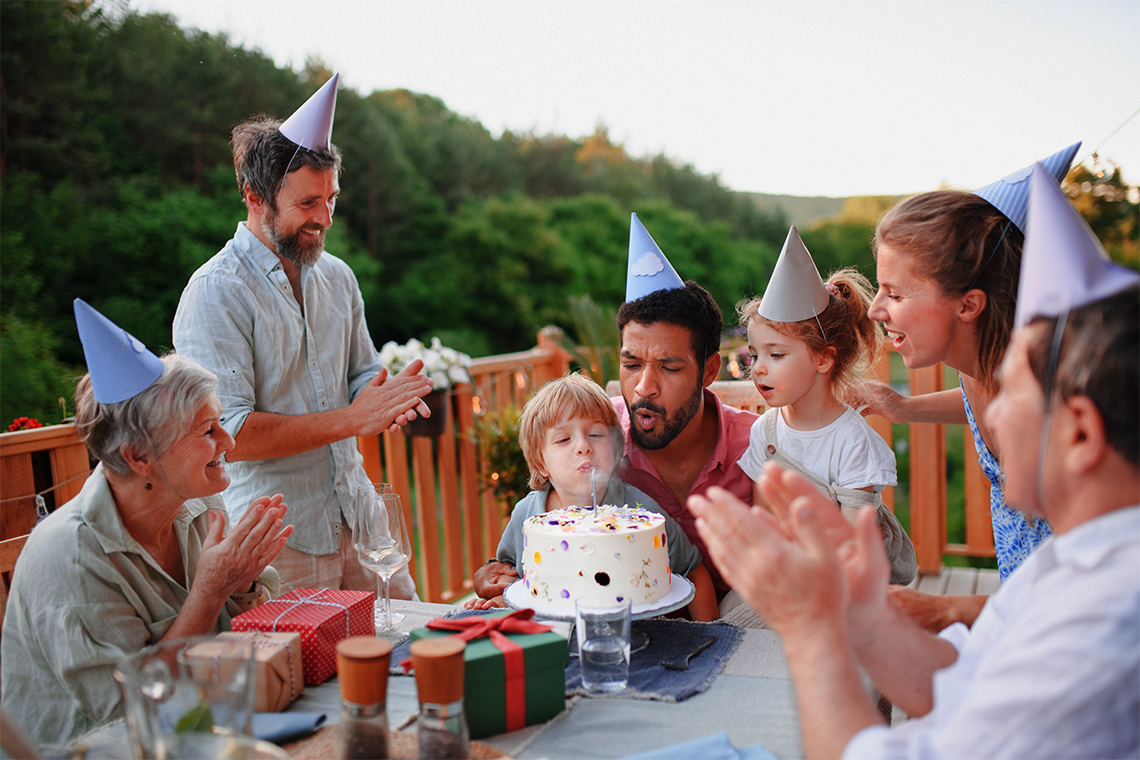 Family and friends at a birthday party. A young kid is blowing out a candle on a birthday cake.