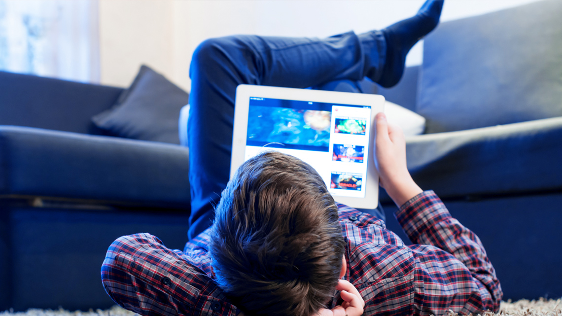 A kid laying down while watching a video on their tablet.