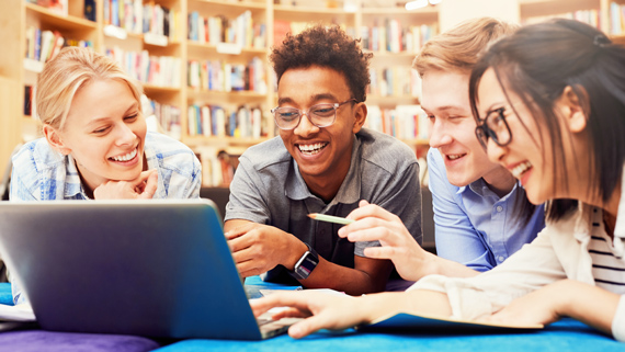 A group of learners laughing in front of a laptop.