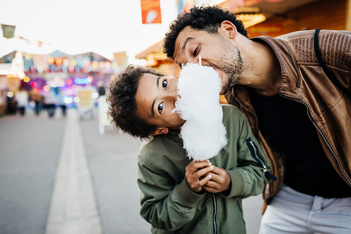 A father and son sharing cotton candy at a festival.