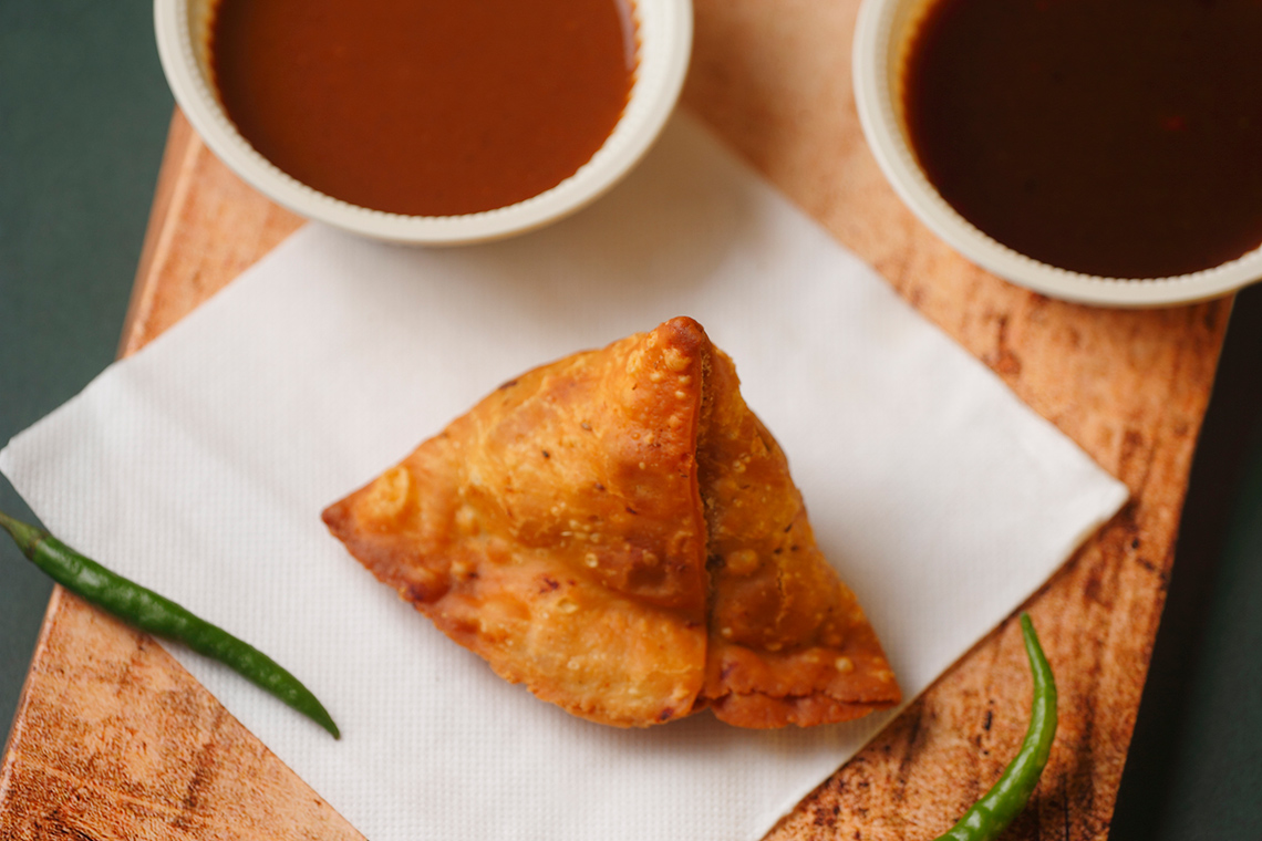 A samosa next to dipping sauce and peppers.