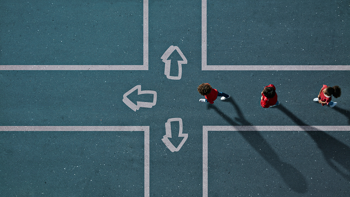 Three students walking on a track in the direction of a west pointing arrow.