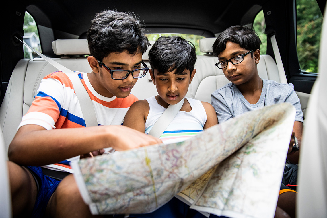 Three boys sitting in a car looking at a large map.