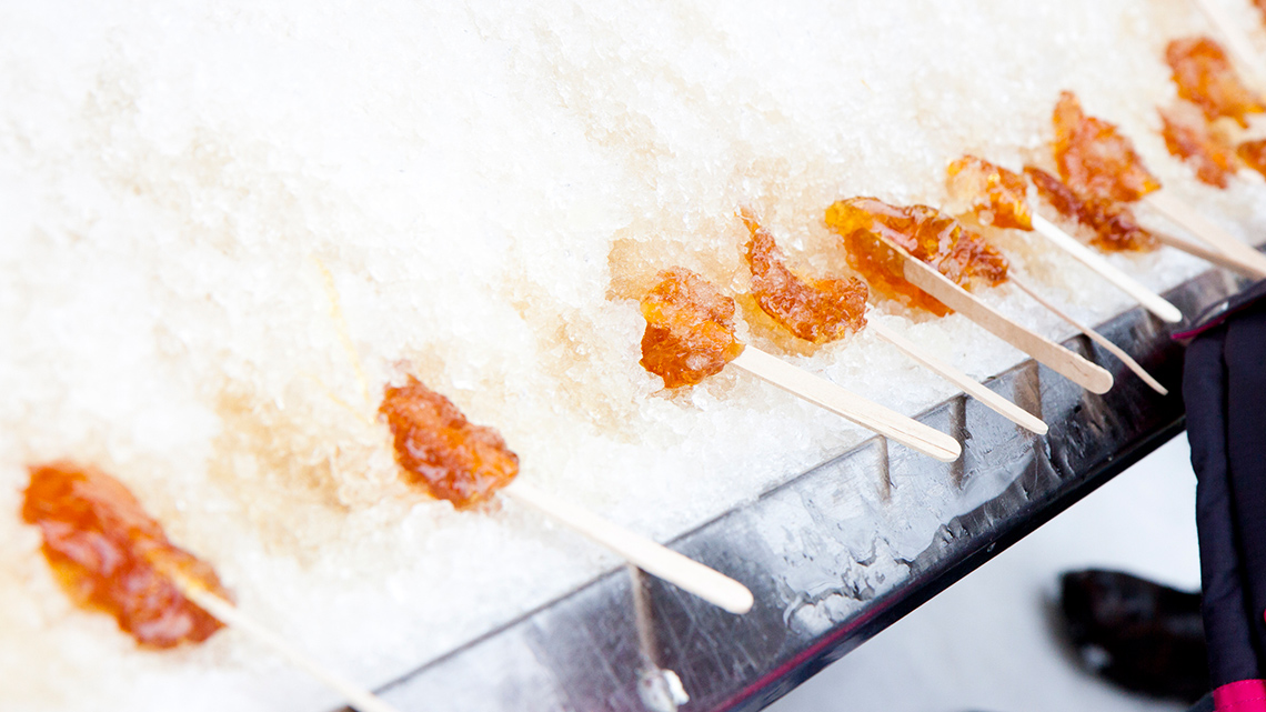 Lumps of maple taffy on popsicle sticks cooling in the snow.