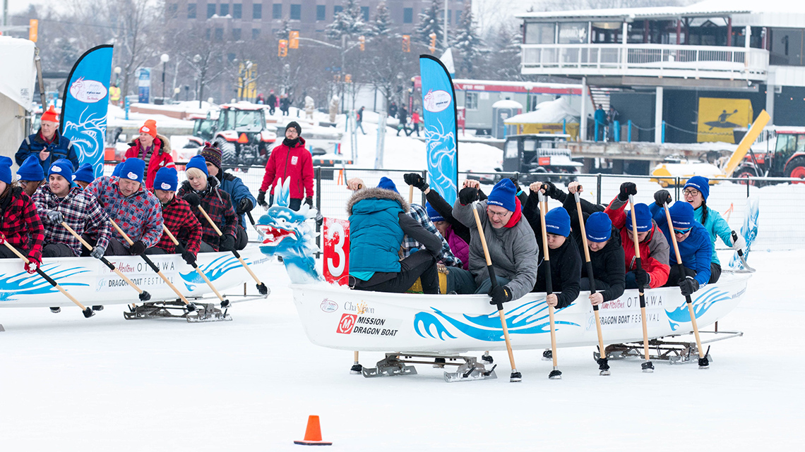 Teams of people racing dragon boats along the ice of the frozen Rideau Canal.