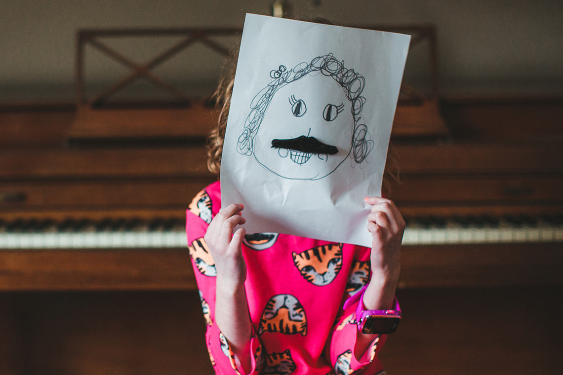 A child covering their face with a drawing of a face.