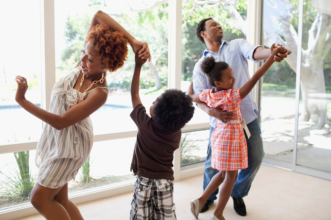 A mother, father, son and daughter dancing inside a home.