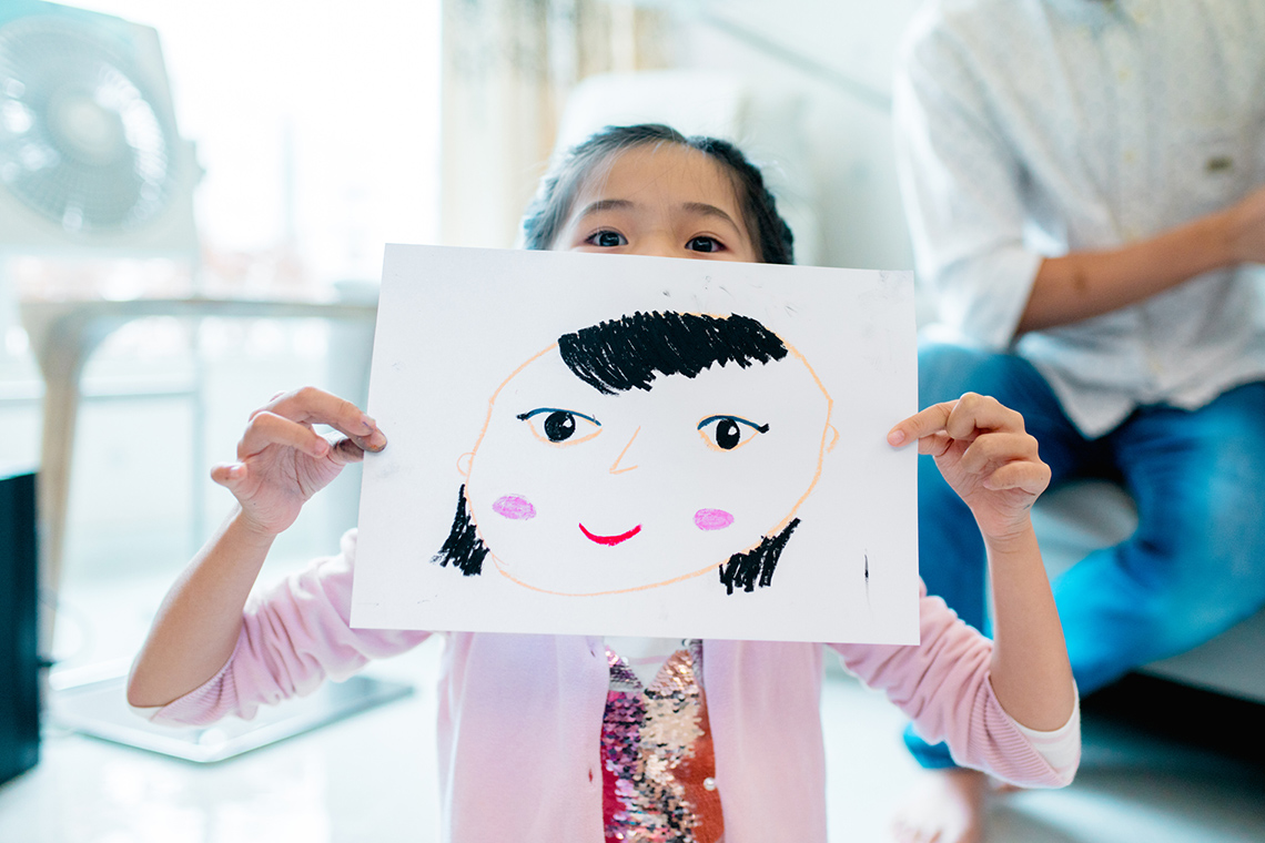 A girl holding up a drawing of a face.