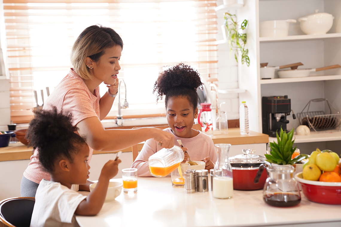 A mom pouring juice for her daughters at breakfast.