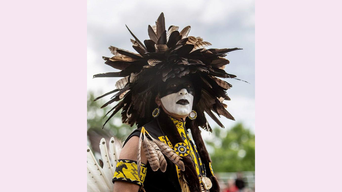 A dancer with a painted face wearing a headdress made of feathers.