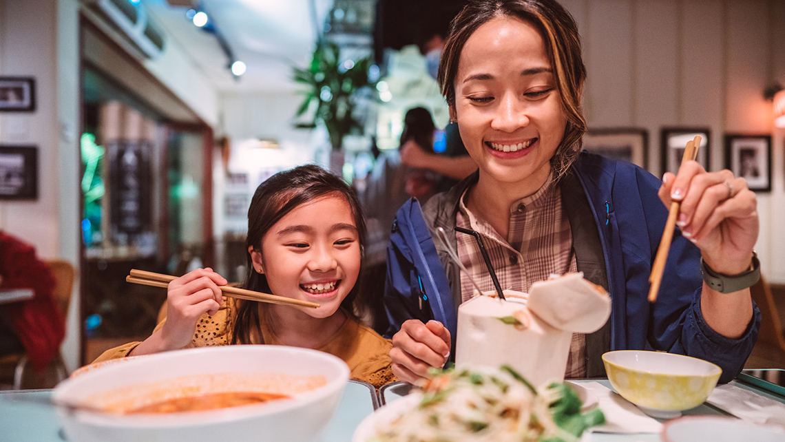 Two people in a restaurant eating with chopsticks.