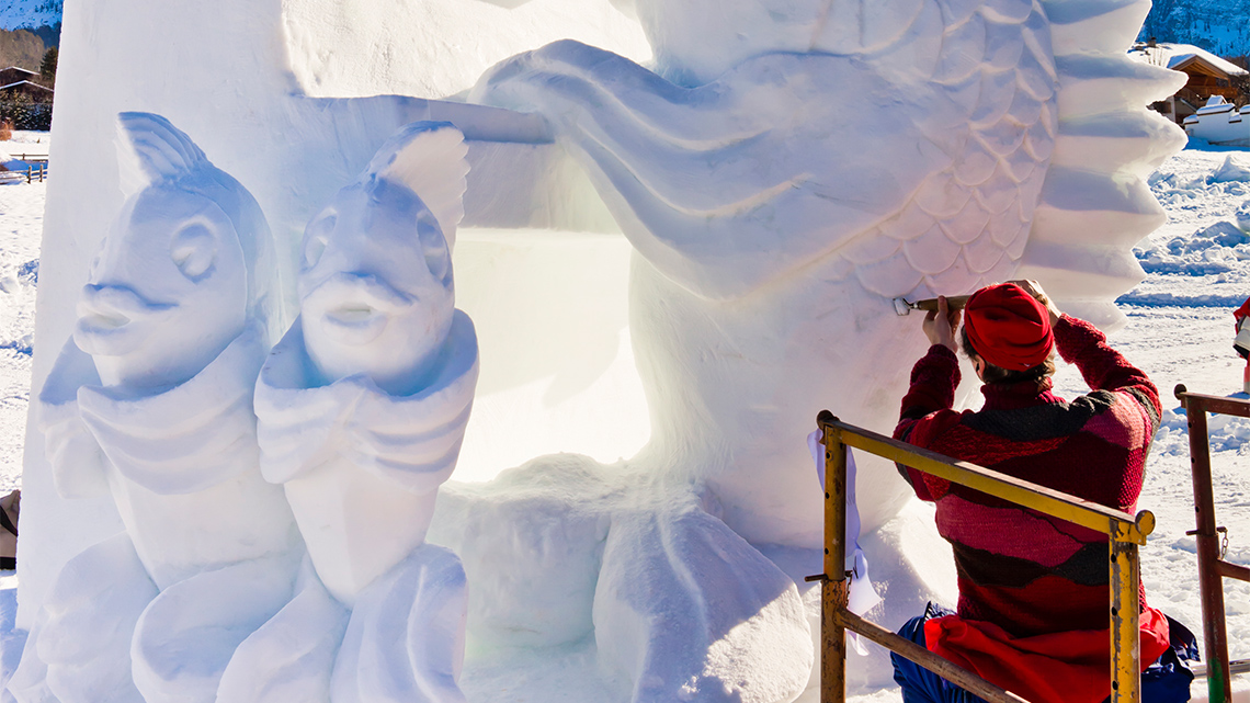 A person using tools to sculpt snow into a decorative sculpture. 