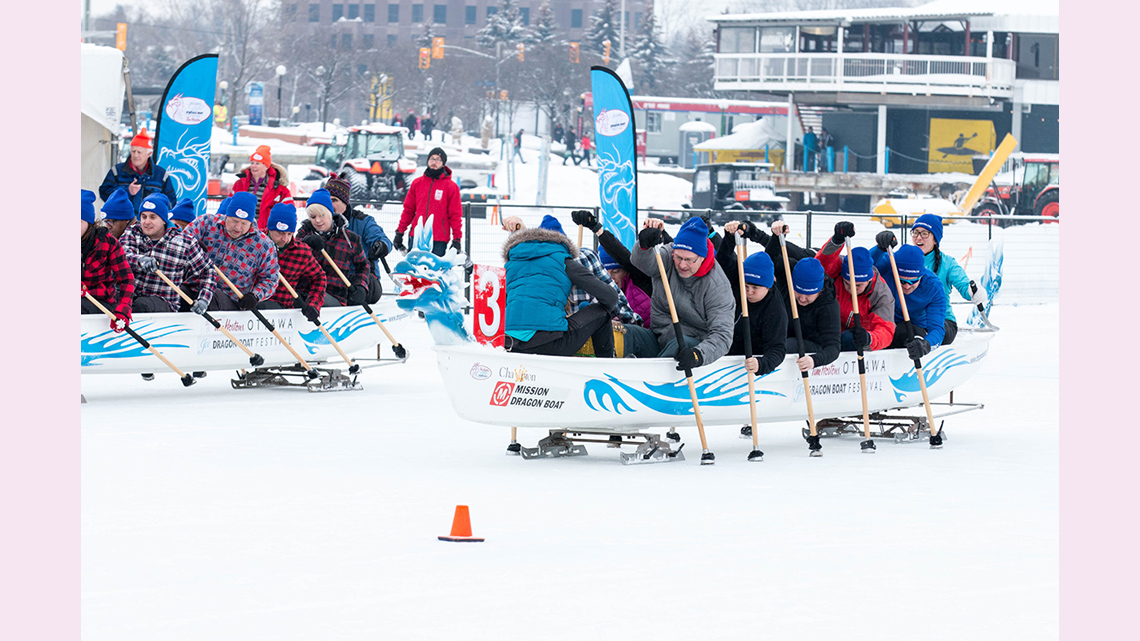 Teams of people racing dragon boats along the ice of the frozen Rideau Canal.