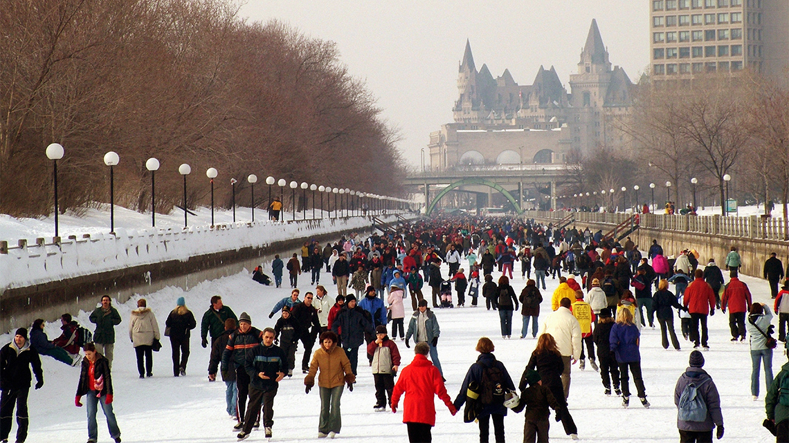 The frozen Rideau canal in winter, with many people skating on the ice.