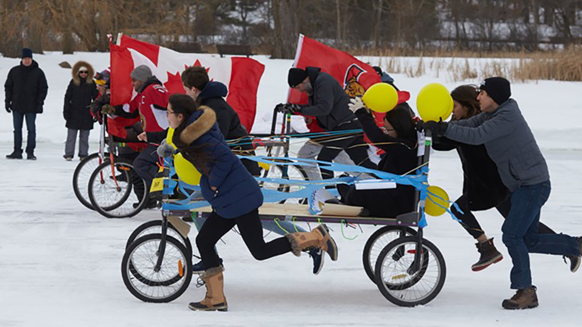 Teams of people push beds mounted to bicycle wheels on the ice of the Rideau canal in winter.