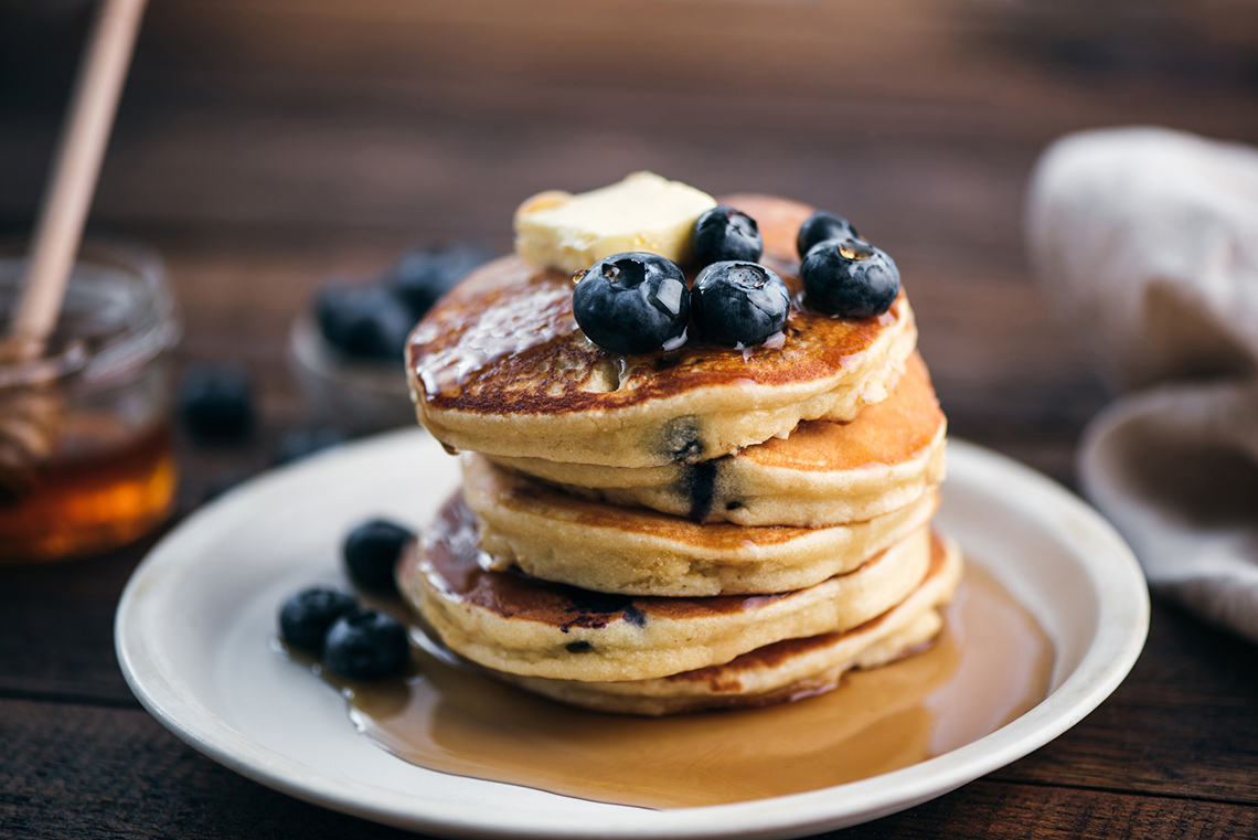 A stack of blueberry pancakes with blueberries, butter and maple syrup on top.