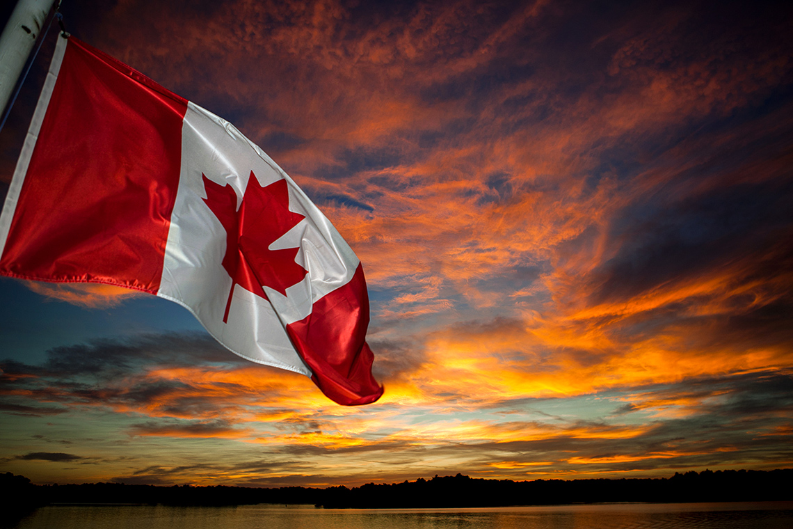 A flag of Canada in the sunset sky.