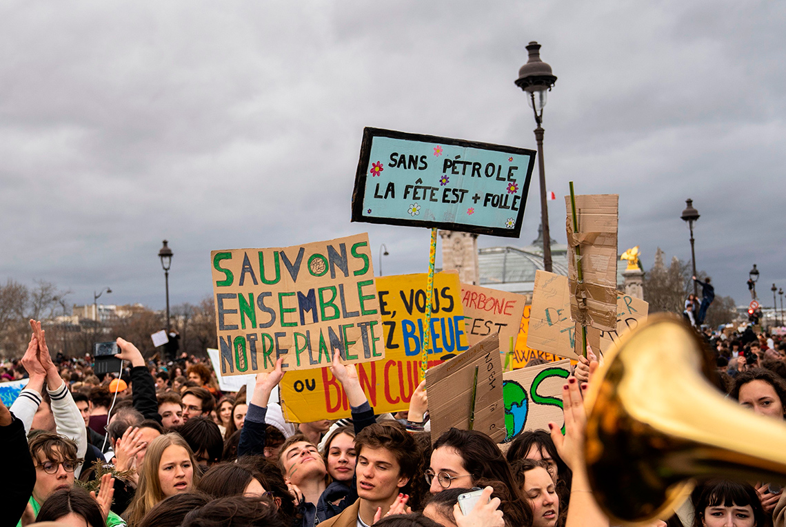 A crowd of environmental demonstrators carry signs that say 'sauvons ensemble notre planète' and 'sans pétrole la fête est plus folle'.