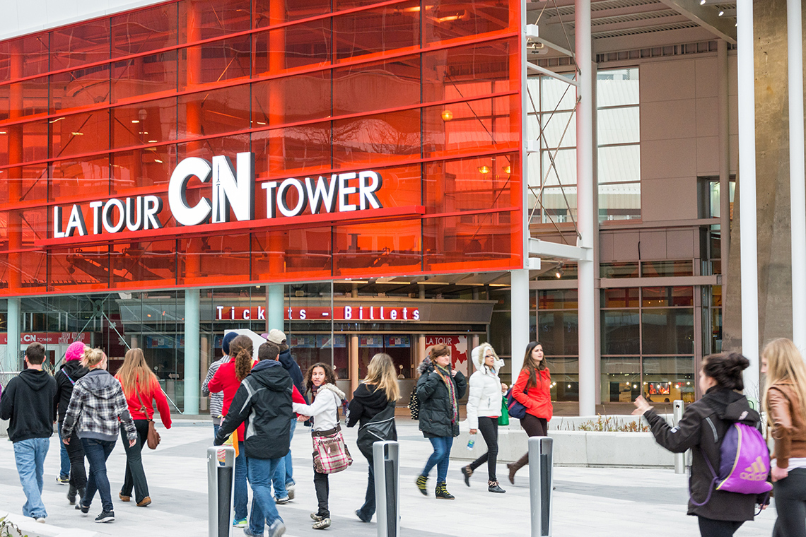 Tourists walking past bilingual signage of the CN tower: la tour CN tower, tickets billets