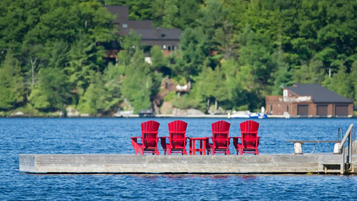 Decolonizing cottage country article thumbnail: 4 red chairs on a dock.