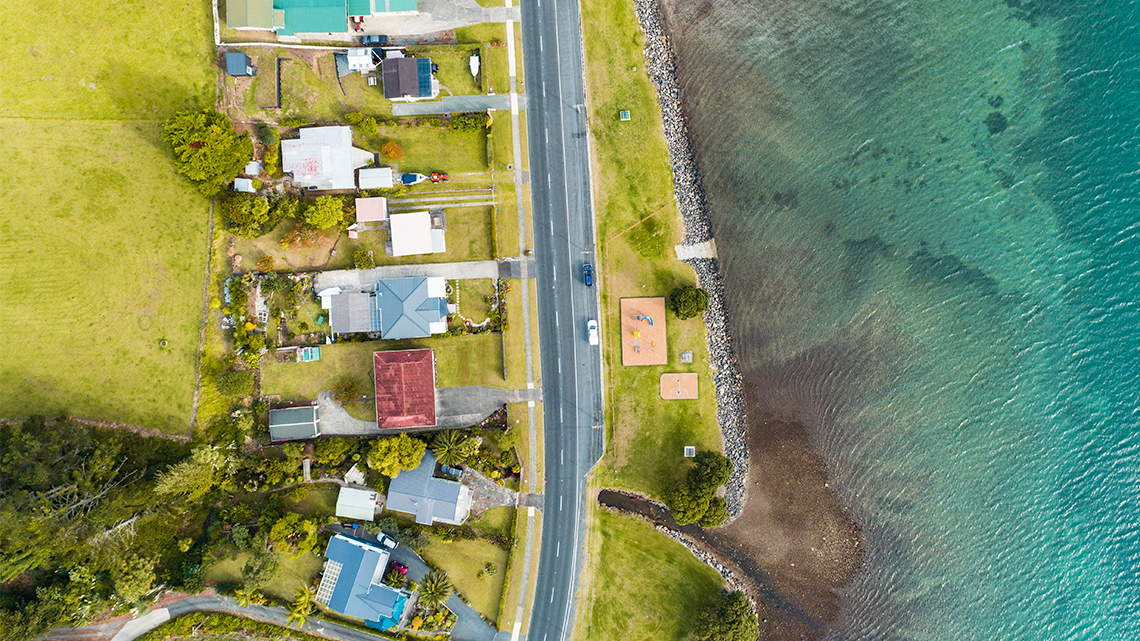 A Settlement in New Zealand A settlement of houses built next to each other along one road and next to a body of water.