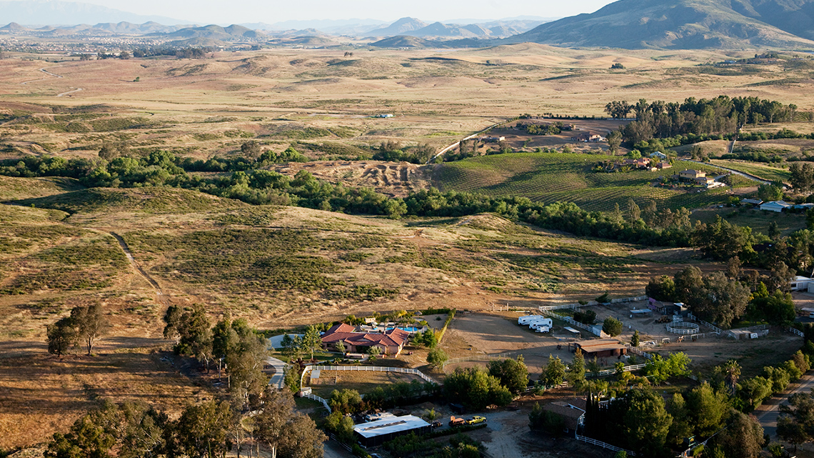 An Aerial View of Farmland This image shows brown land and a few trees with a few houses built far apart from each other.