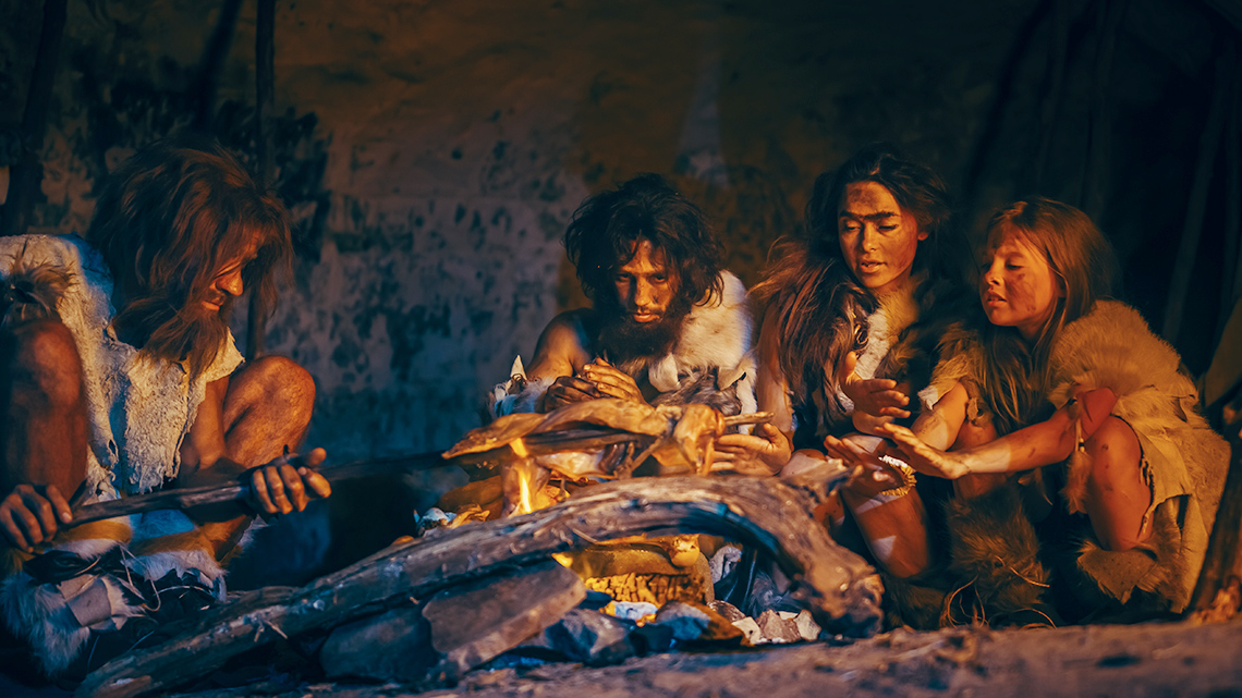 A group of hunters and gatherers sit around a fire at night.