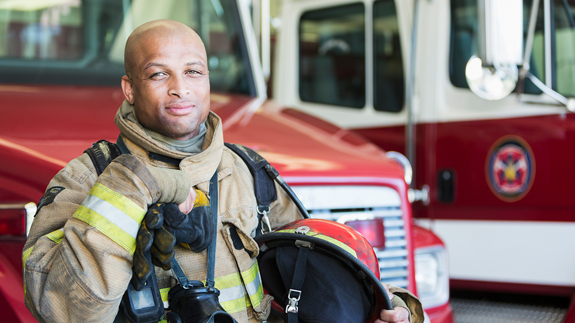 A firefighter stands in his uniform in front of a fire truck