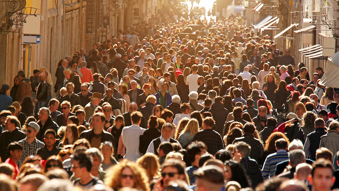 A city street crowded with people between two rows of buildings.