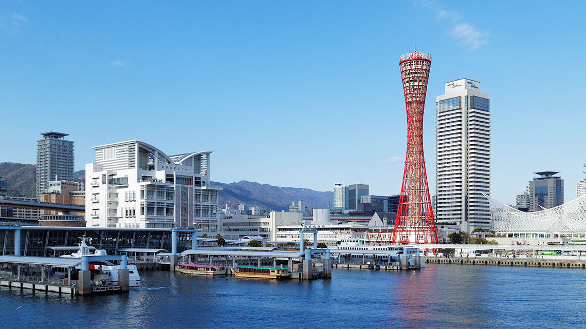 An image of the skyline of skyscrapers in Kobe, Japan on the water with a boat at the port.