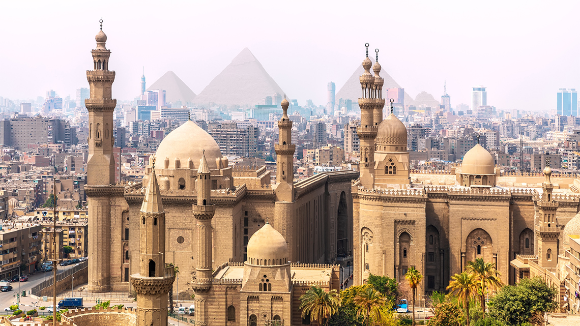 An image of Cairo, Egypt with a mosque with minarets, multi-story buildings, and 3
                                pyramids.