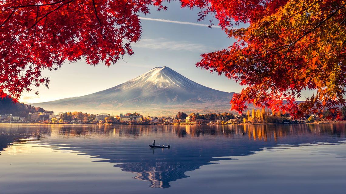 The Colourful Autumn Season at Mount Fuji and Lake Kawaguchiko An image of a lake with red maple tree leaves, and a volcanic mountain in the
background.