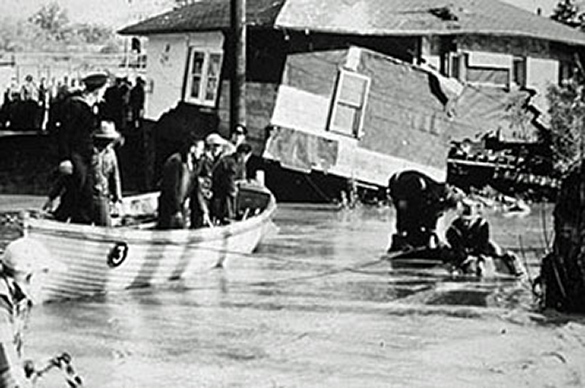 People in a small boat in a flooded street searching for other people to rescue.