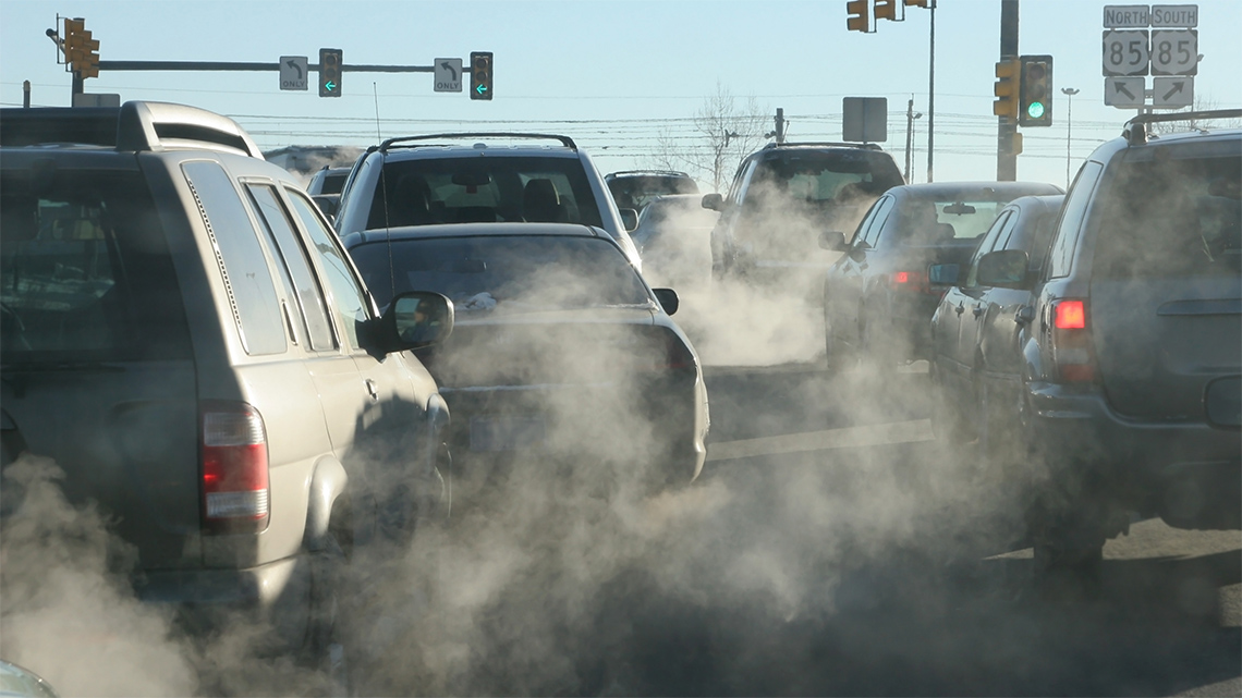 As cars are driving towards a green light, exhaust clouds surround the cars.